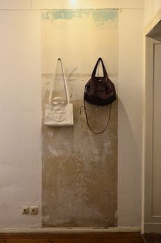 White and dark feminine handbags hanging on hooks on shabby wall with sockets in light room near doorway at home