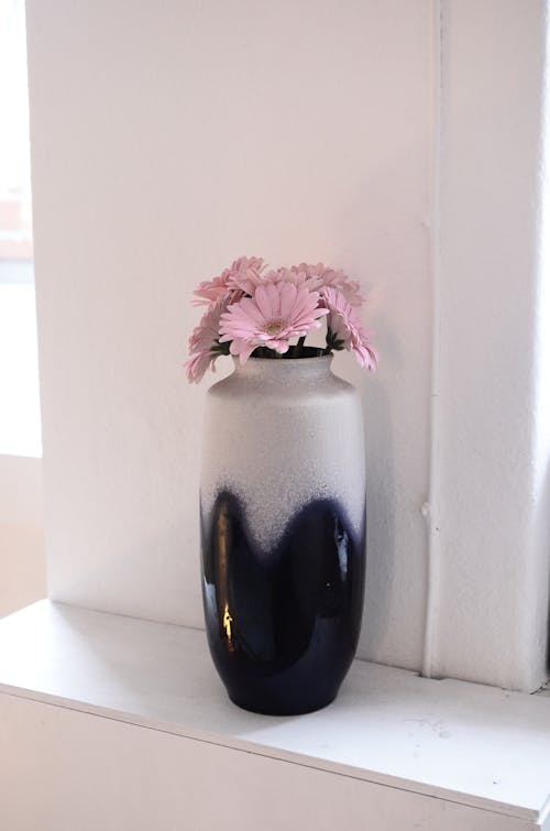Vase with pink flowers near wall
