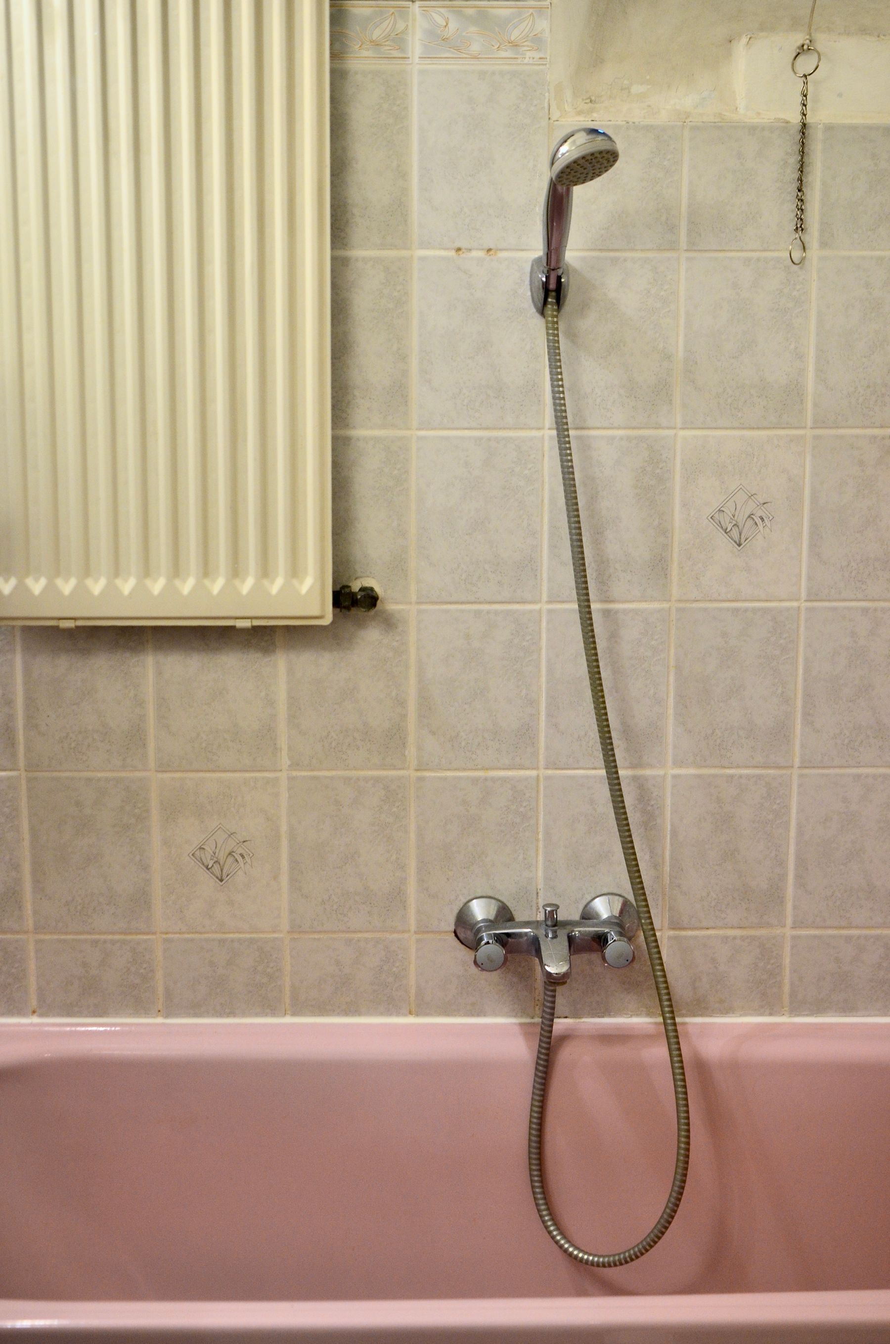 Pink bath with chrome wall-mounted shower, pale square tile and a cream curtain