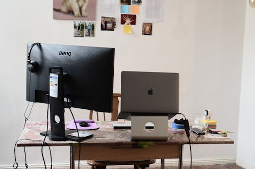 Free Black monitor with headphones placed on desk with modern netbook on stand against wall with photos at convenient workplace in room Stock Photo