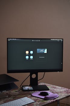 A sleek desktop setup featuring a monitor, keyboard, and mouse on a patterned tablecloth.