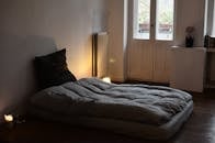 Comfortable mattress with blanket and cushion placed on wooden floor in dark bedroom with burning candles and flowers in vase