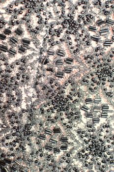 Background of textured textile with creative ornament and various dark sequins and beads creating abstract pattern on stylish gray cloth