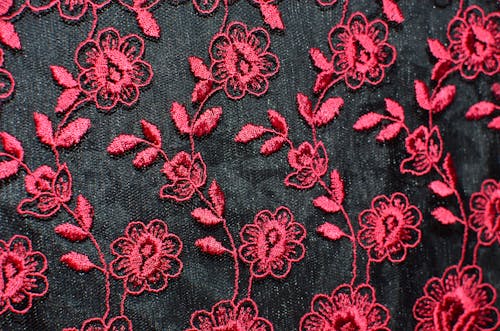 Seamless background of creative flowers with leaves embroidered on black fabric with red thread creating symmetrical pattern on thick textile