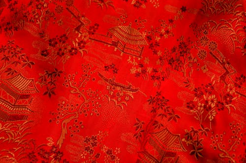 Background of bright fabric with oriental design of tree and floral pattern with traditional huts elements on thick decorated textile