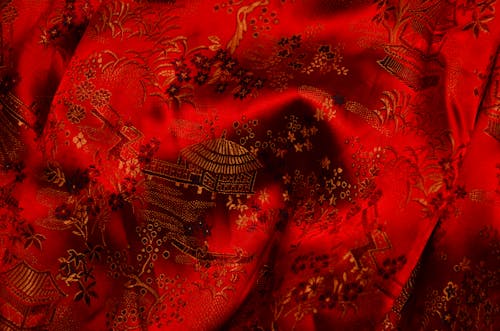 Background of bright fabric with authentic oriental ornaments of floral patterns and traditional huts on creased surface of red textile