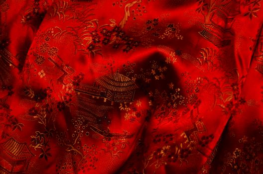 Background of bright fabric with authentic oriental ornaments of floral patterns and traditional huts on creased surface of red textile
