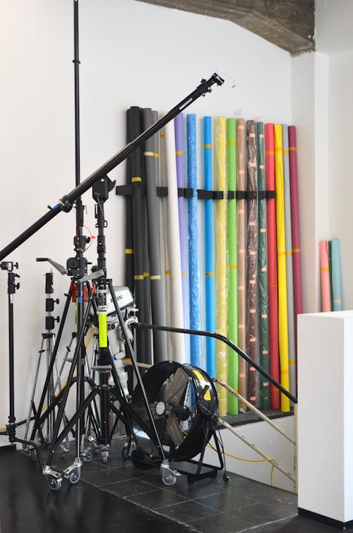 Collection of rolled bright fabric placed at white wall in modern studio with tripods and professional equipment during photo shoot