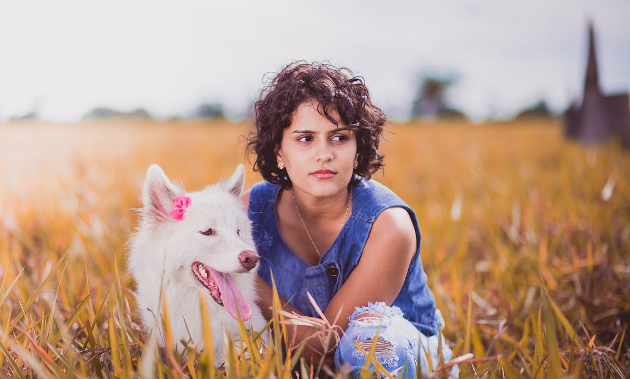 Woman Squatting Near White Dog on Grass Field