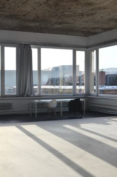 Chairs and table placed near big window with curtain with modern buildings view in empty minimalistic room with bright sunlight