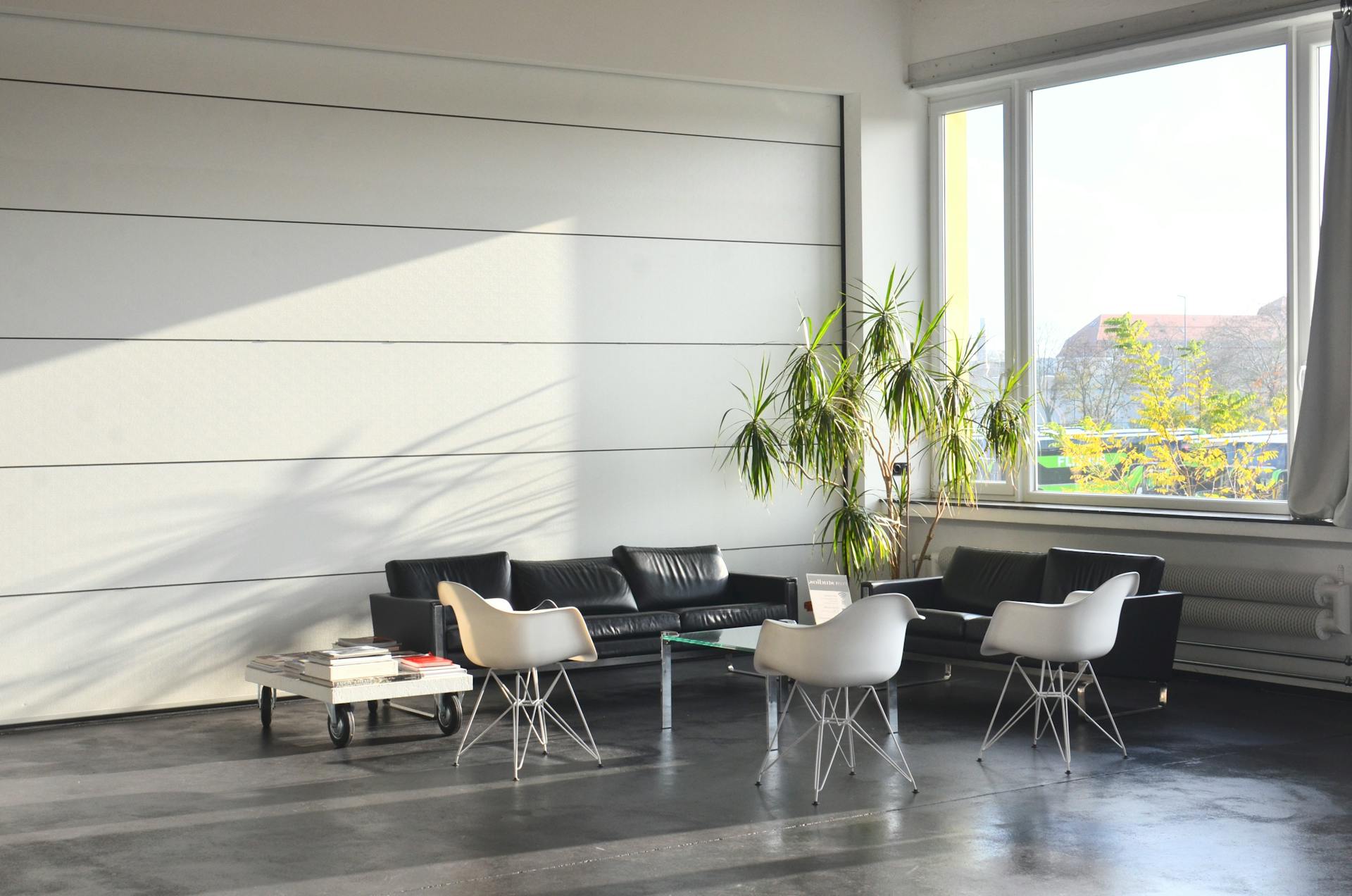 Interior of light modern lobby with sofas and armchairs placed near side table at wall near window with potted plant