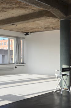 Spacious modern loft with natural light and minimalist design featuring a white chair and pillar.