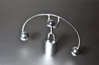 Stainless weightlifter kinetic perpetual dynamic motion toy with balance balls placed on gray table in light room on blurred background