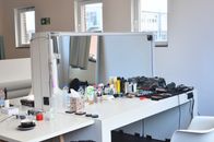 White dressing table with cosmetic products and instruments near table with coffee placed in light room with windows and mattress
