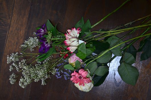 Top view of fresh pink gerberas roses purple alstroemeria and gypsophila on green stems with leaves placed on wooden table