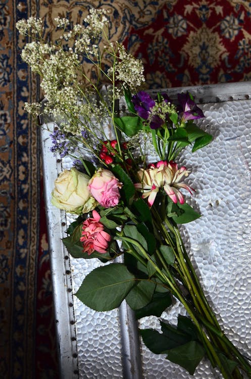 Top view of fresh roses alstroemeria and gypsophila flowers on long stems with leaves placed on white metallic structure on carpet