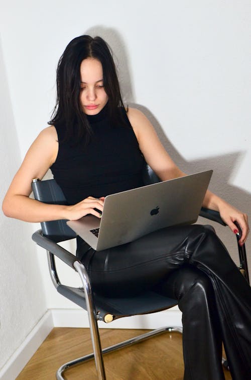 Wanita Dengan Tank Top Hitam Duduk Di Kursi Menggunakan Macbook