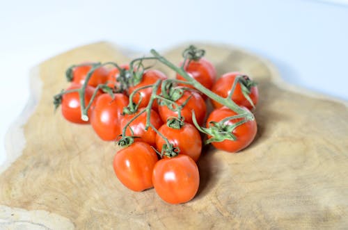 Free Red ripe cherry tomatoes on green vine placed on wooden cutting board on white table in light room on blurred background Stock Photo