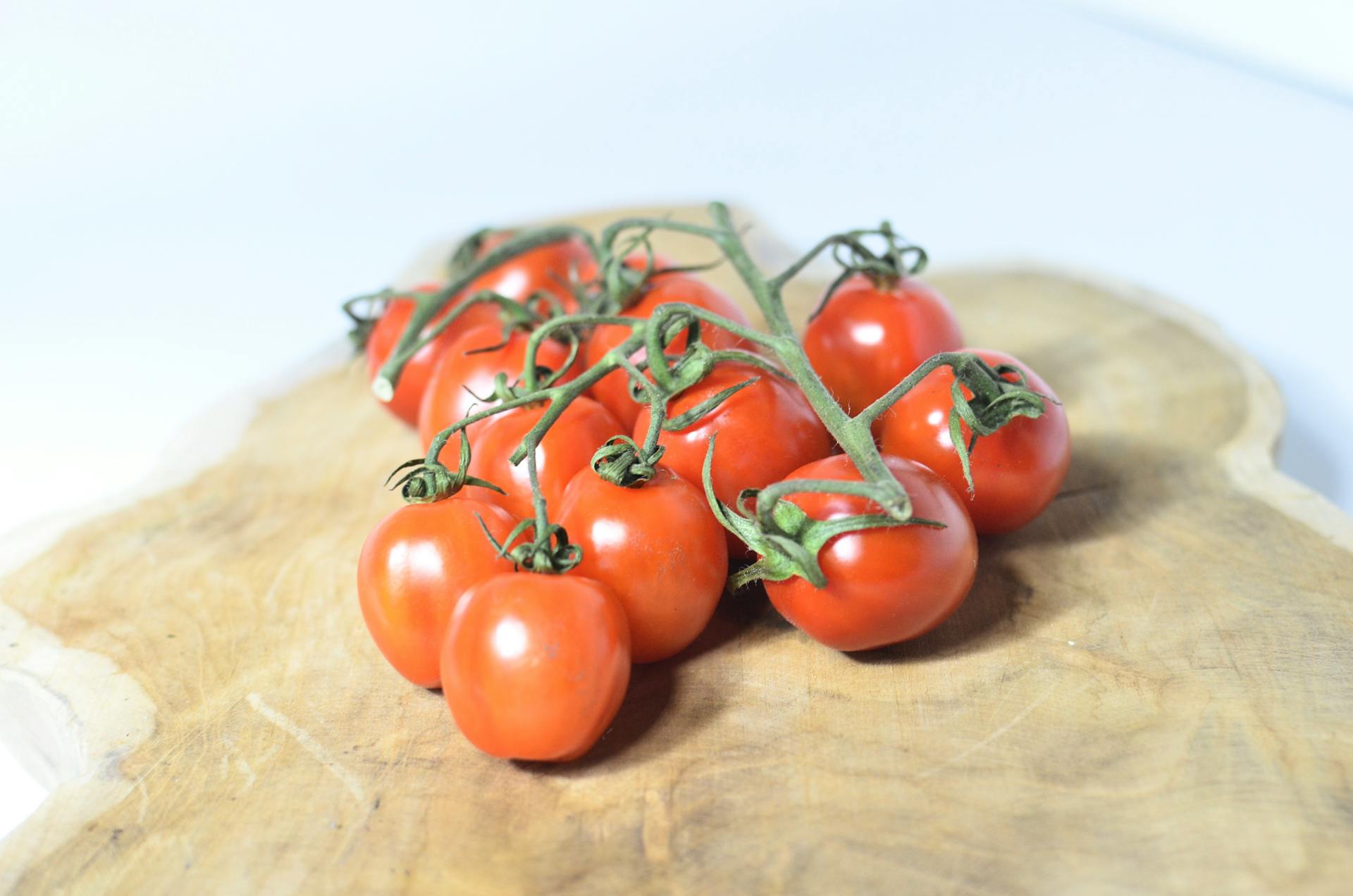 Small fresh red cherry tomatoes on green branch placed on shaped wooden cutting board on white table in light room