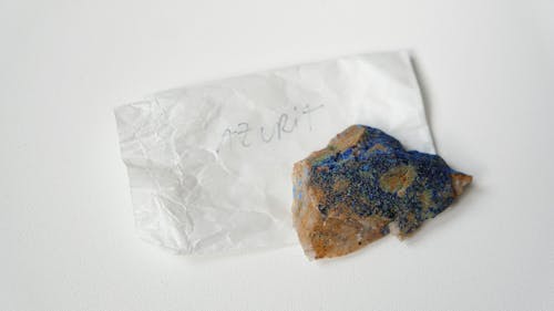 From above of multicolored stone Azurite placed on small sheet of paper with inscription on  white table