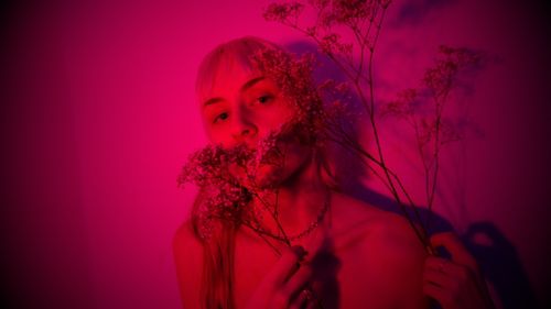 Free Thoughtful woman without clothes standing with sprig of plant in room illuminated by neon and looking at camera Stock Photo