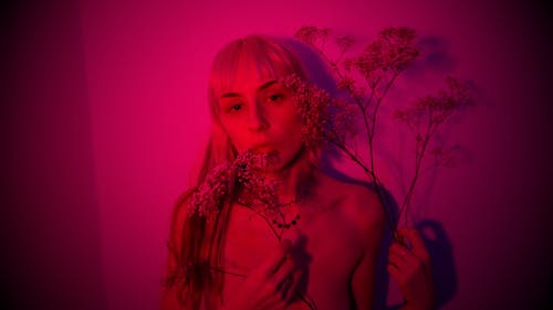 Sensual woman holding sprig of plant in room with neon light