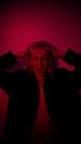 Frightened young female in black wear crying touching head with closed eyes standing in dark room illuminated with purple neon light