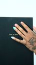 Top view of crop unrecognizable informal female with colorful manicure and tattoos with Come To Berlin book with black hardcover