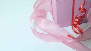 From above of pink cardboard present box decorated with colorful ribbons on gray background