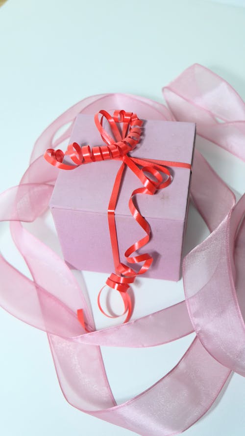 From above of pink cardboard present box tied with red band bow and ribbon on gray background