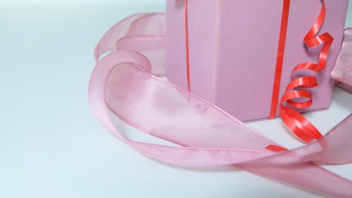 High angle of pink gift box tied with red band and decorated with ribbon on gray background