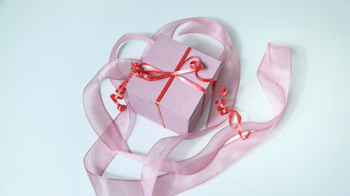 From above of pink cardboard gift box tied with red band and decorated with ribbon on gray background