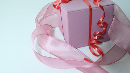 From above of pink carton present box decorated with ribbon and tied with red band on gray background