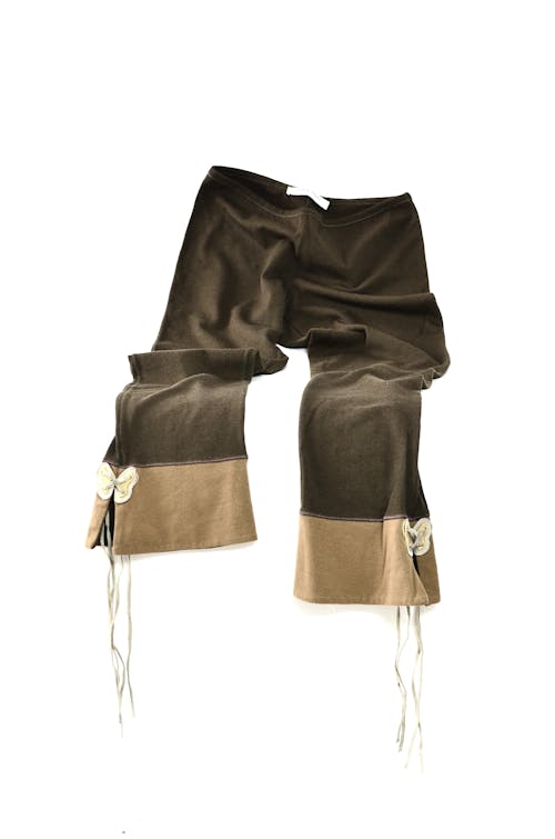 Brown peculiar pants with bows and laces at bottom on white background in studio