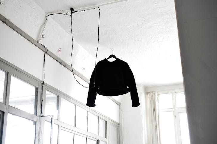 From below of simple black sweater hanged on ceiling in white room with glass windows