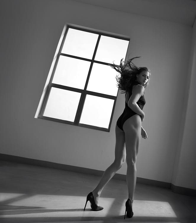 Sensual woman in bodysuit standing in empty room