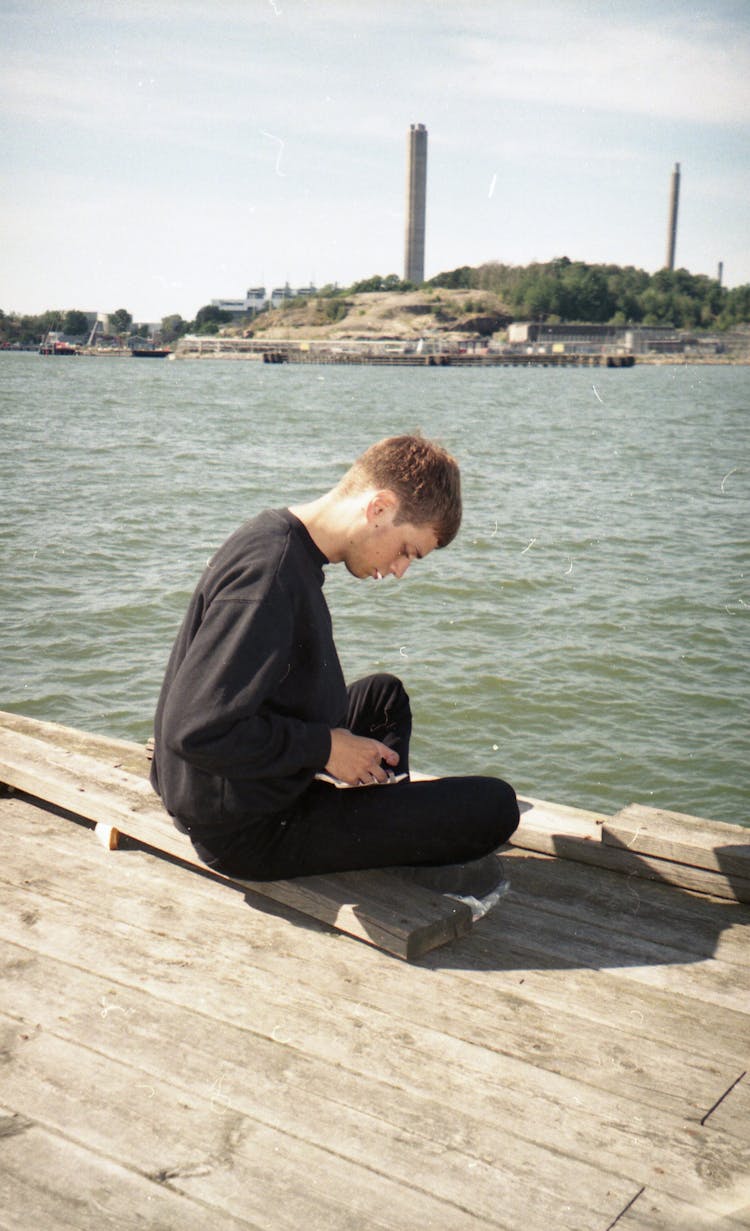 Young Man Sitting On Pier Near Sea