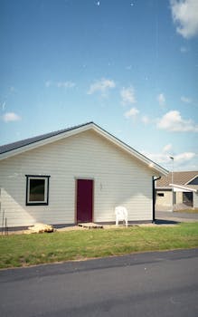 A quaint suburban house with a red door, situated in a peaceful neighborhood under a clear blue sky.