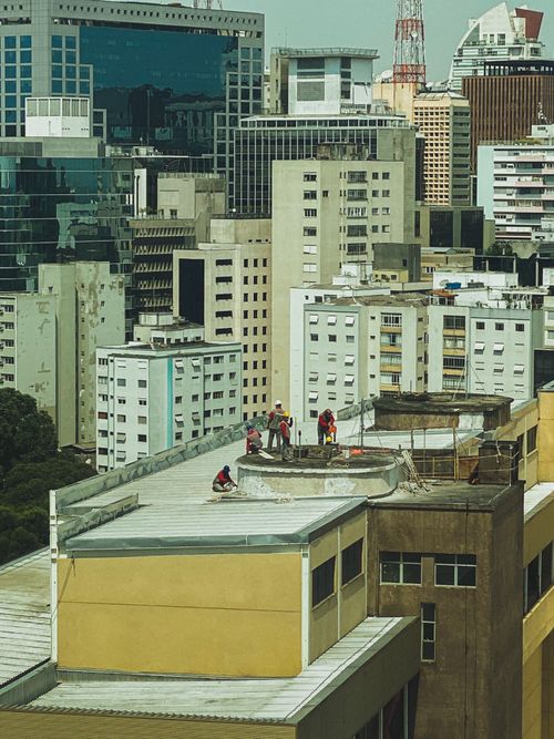 Free View of construction workers on a rooftop amid high-rise buildings in a bustling city. Stock Photo