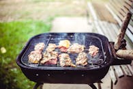 在阳光明媚的户外野餐中，木炭烤架上多汁的牛肉和鸡肉正嘶嘶作响