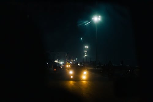 Through windshield glass of various cars with glowing headlights driving on asphalt road in city against dark night sky