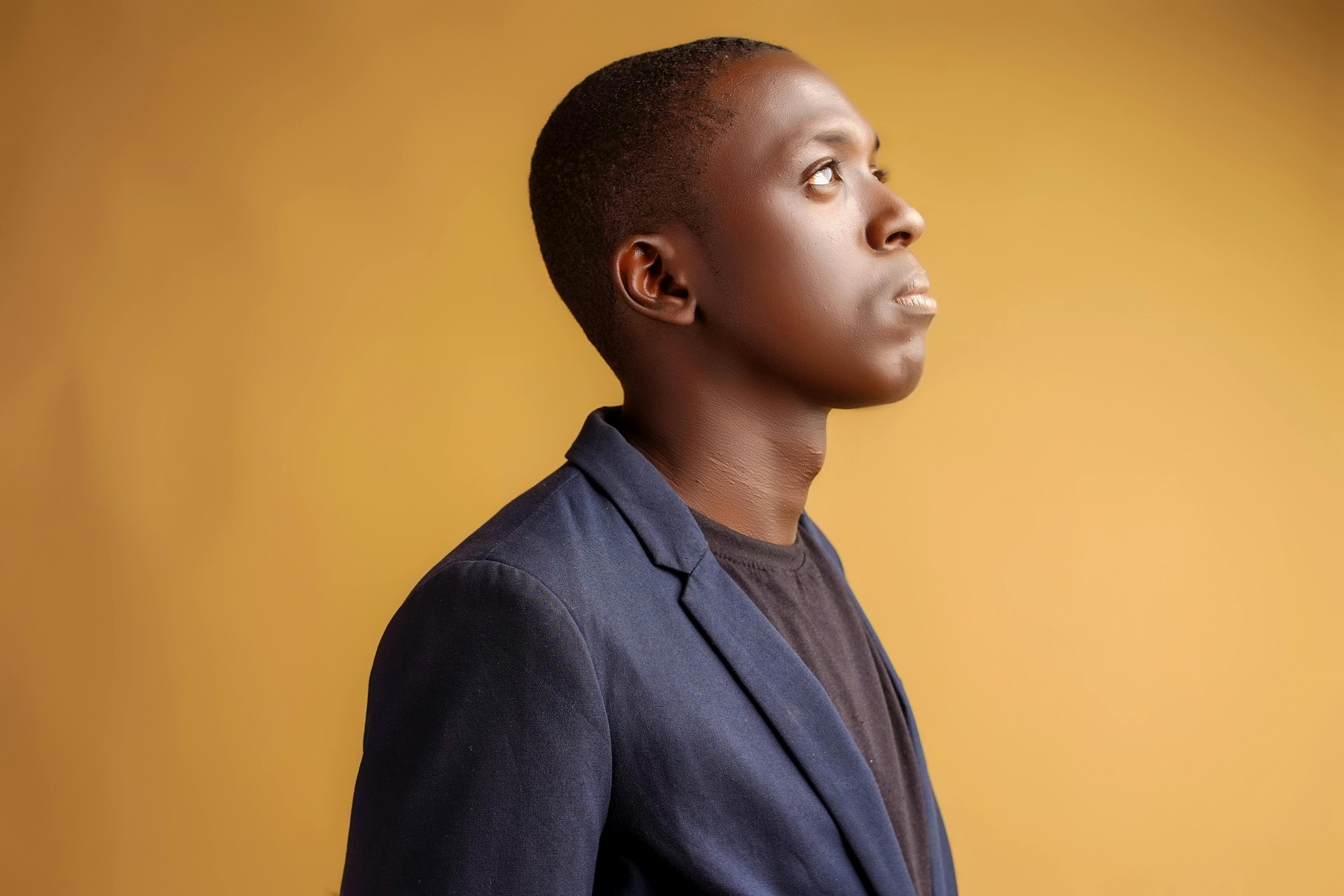 A young African American man in a blue blazer looking upward against a yellow background.