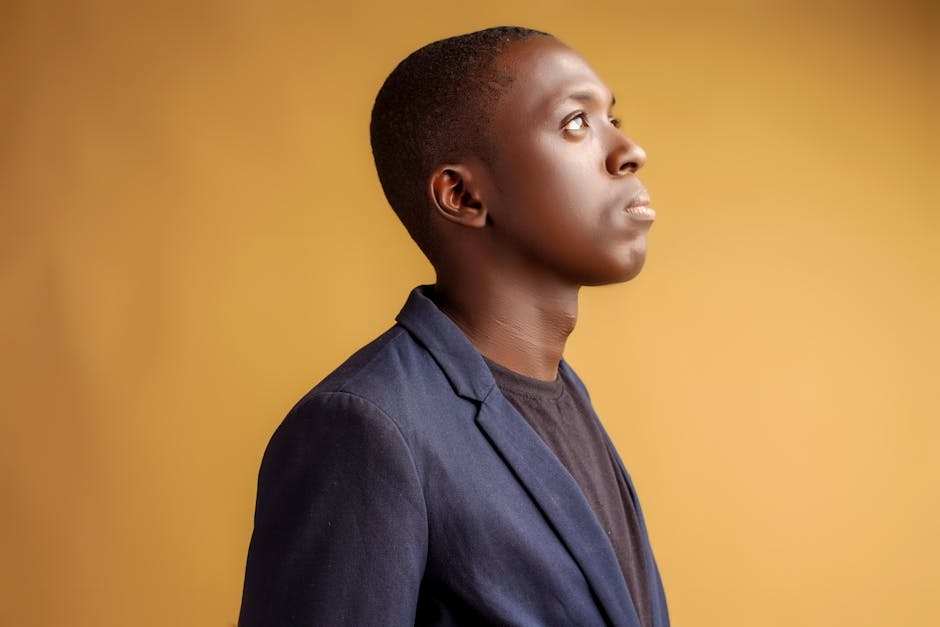 A young African American man in a blue blazer looking upward against a yellow background.