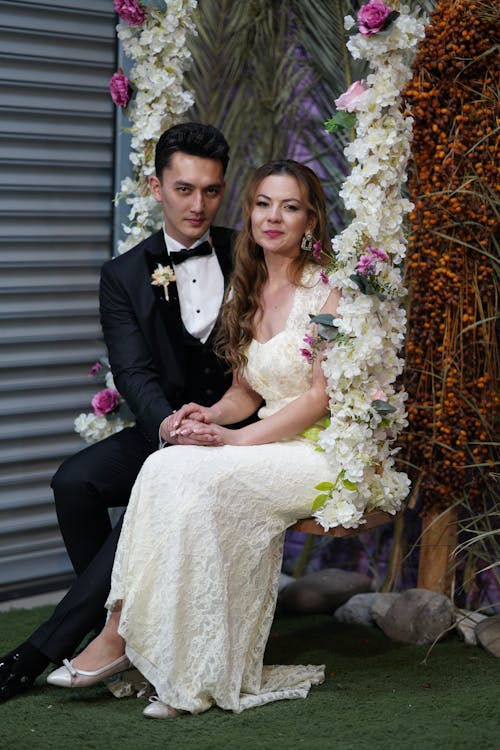 Woman in White Wedding Gown Sitting Beside Man in Black Suit