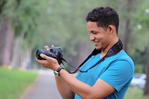 Free Casual photo of a smiling man using a camera in a green park setting. Stock Photo