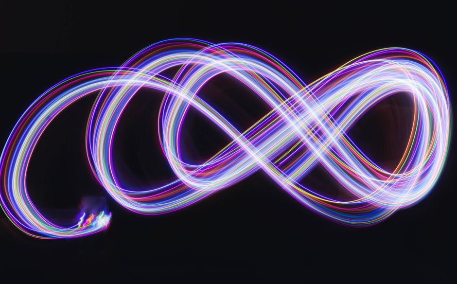 Abstract long exposure photography of colorful neon light streaks forming an infinity symbol.