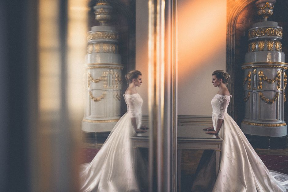 Bride in wedding gown looking at her reflection in an ornate mirror