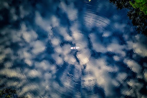 An Aerial Shot of a boat in the Water with Reflection of Clouds and Trees