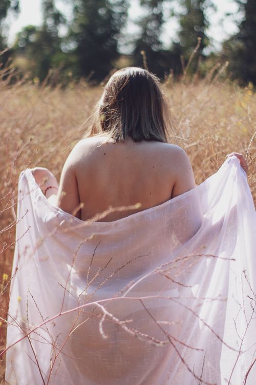 Free A calming image of a woman from the back, draped in soft fabric amidst tall grass. Stock Photo