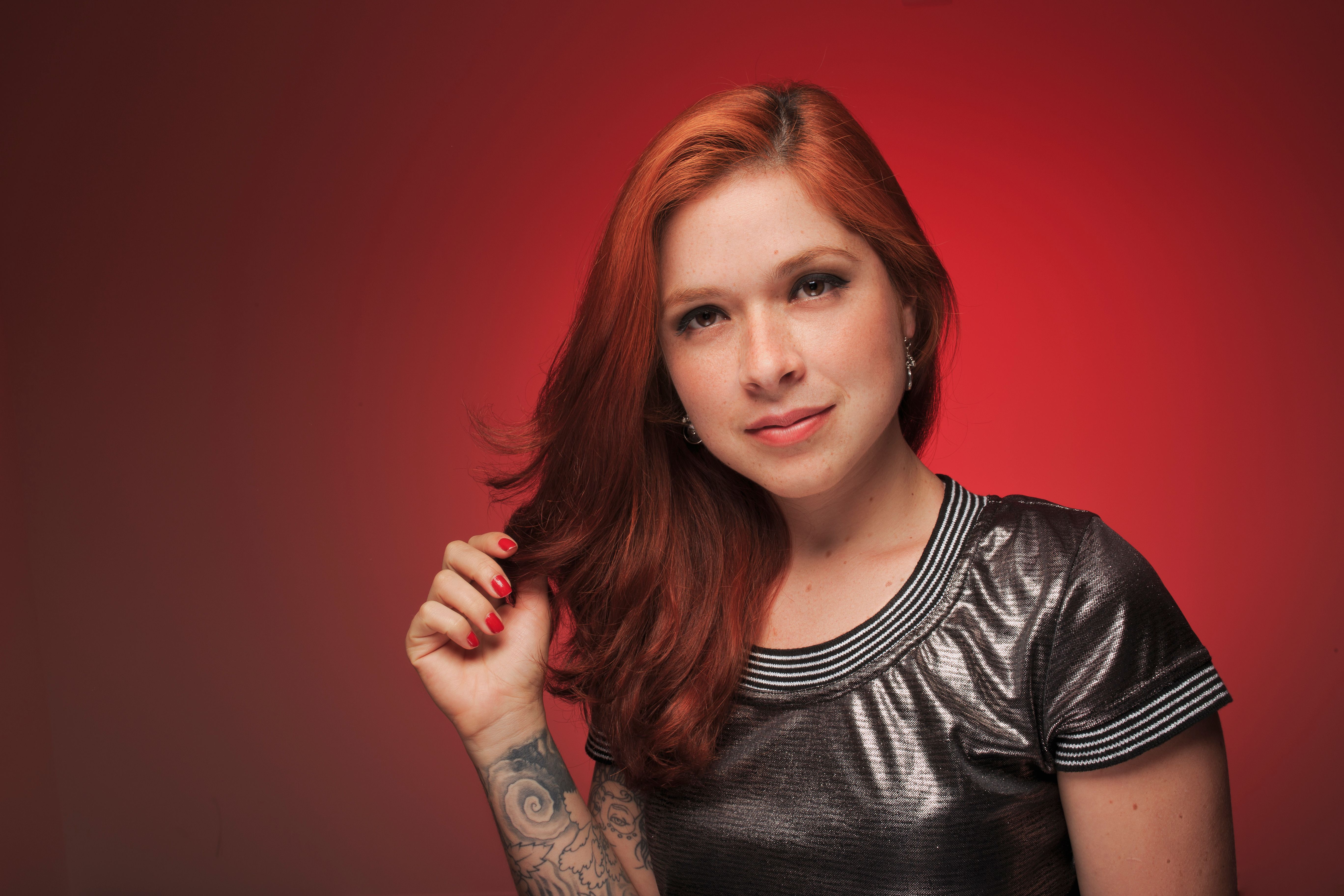 Stylish portrait of a young woman with red hair and tattoo on a red background.